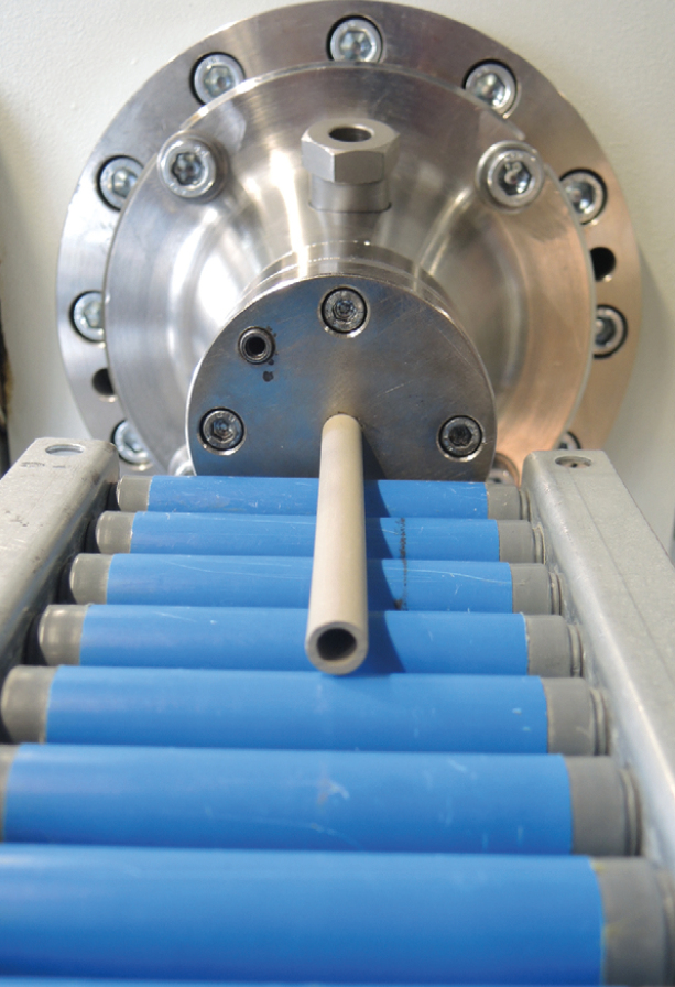 Erdfarbene keramische Röhre auf einem Rollband vor einem Extrusionswerkzeug.