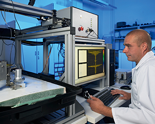 Eine Person sitzt in einem Labor und führt eine Ultraschallprüfung an einem GfK-Verbundbauteil durch