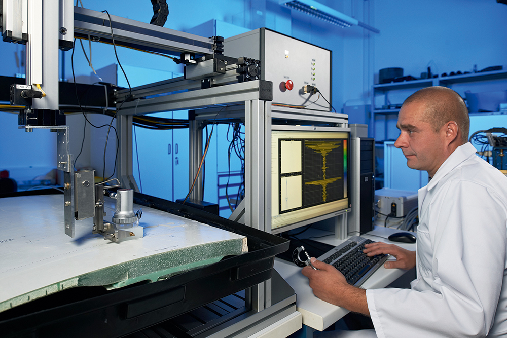 Eine Person sitzt in einem Labor und führt eine Ultraschallprüfung an einem GfK-Verbundbauteil durch