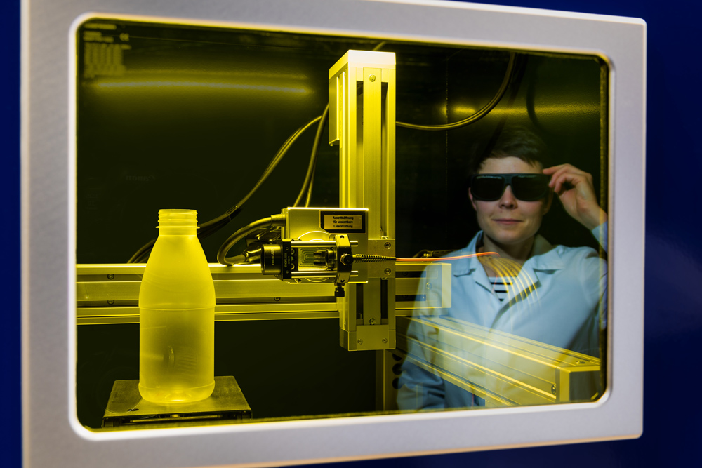 Durch ein Fenster ist  der zweiter Prototyp eines Diagnosesystems (OCD) für die optische Krebsdiagnose zu sehen und in der Reflektion sieht man eine Person die mit einer verdunkelten Brille den Prototyp betrachtet.