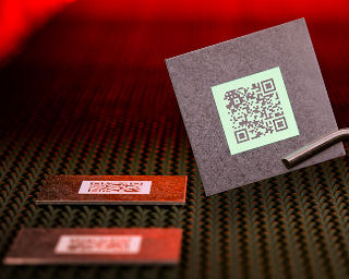 Hochtemperaturfähige Produktmarkierung in Form eines QR-Codes auf Bauteil unter UV-Licht gehalten.